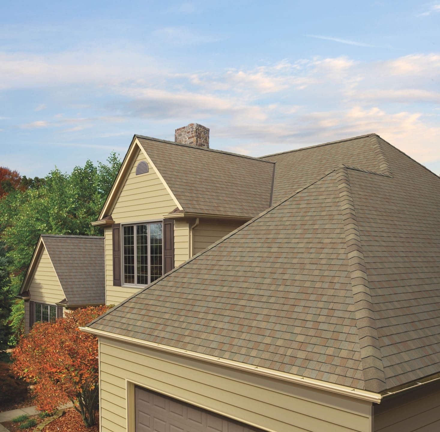 Two-story house with beige siding and brown shingle roofing, framed by autumn trees.