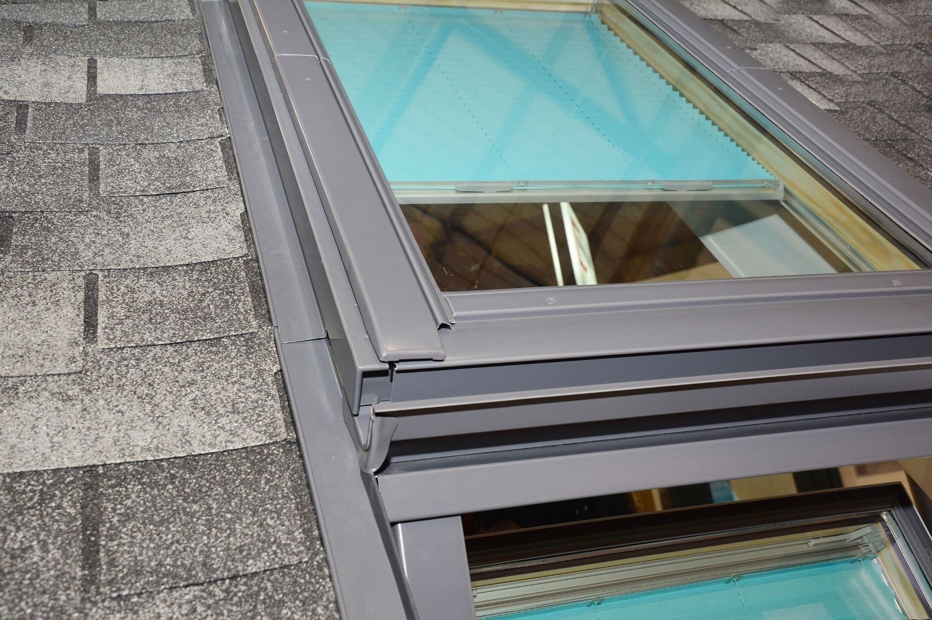 Close-up of a roof showing grey asphalt shingles and a skylight window with built-in blind.